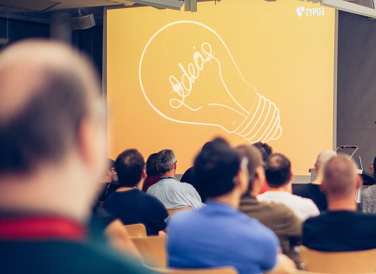 Audience from behind, looking at projection screen with white lightbulb and word "idea" on orange background.